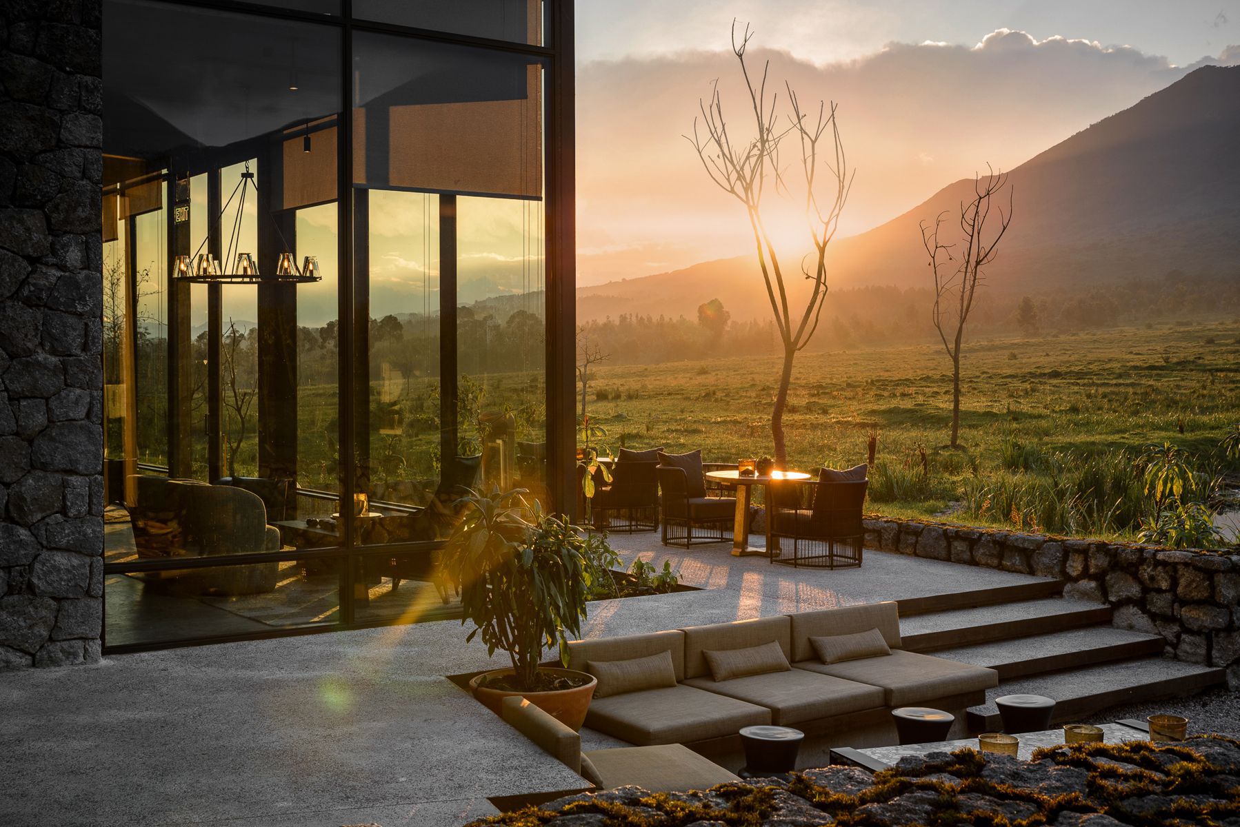 Hotel patio overlooking a green, grassy field as the sun sets in warm, glowing colors over a mountain range in the distance.