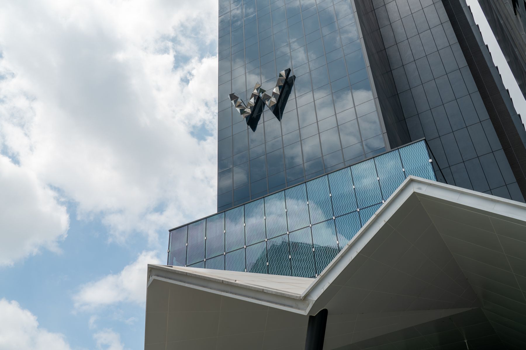 An exterior view of the W Chengdu hotel, showcasing glass windows, the W logo, and a blue, cloud-filled sky.