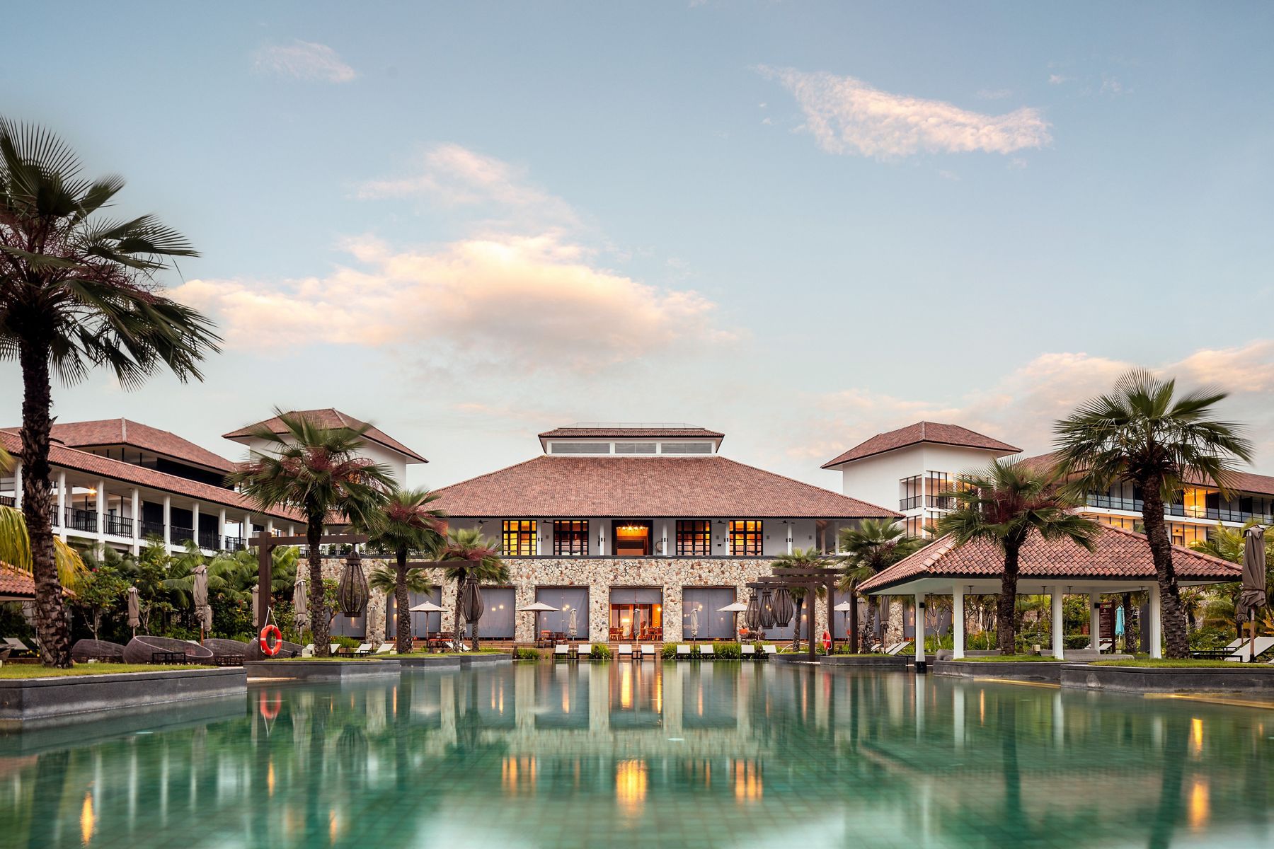 An exterior view of the Anantara Desaru Coast Resort in Johor, Malaysia, showcasing a stunning blue lagoon with palm trees and beachside villas.