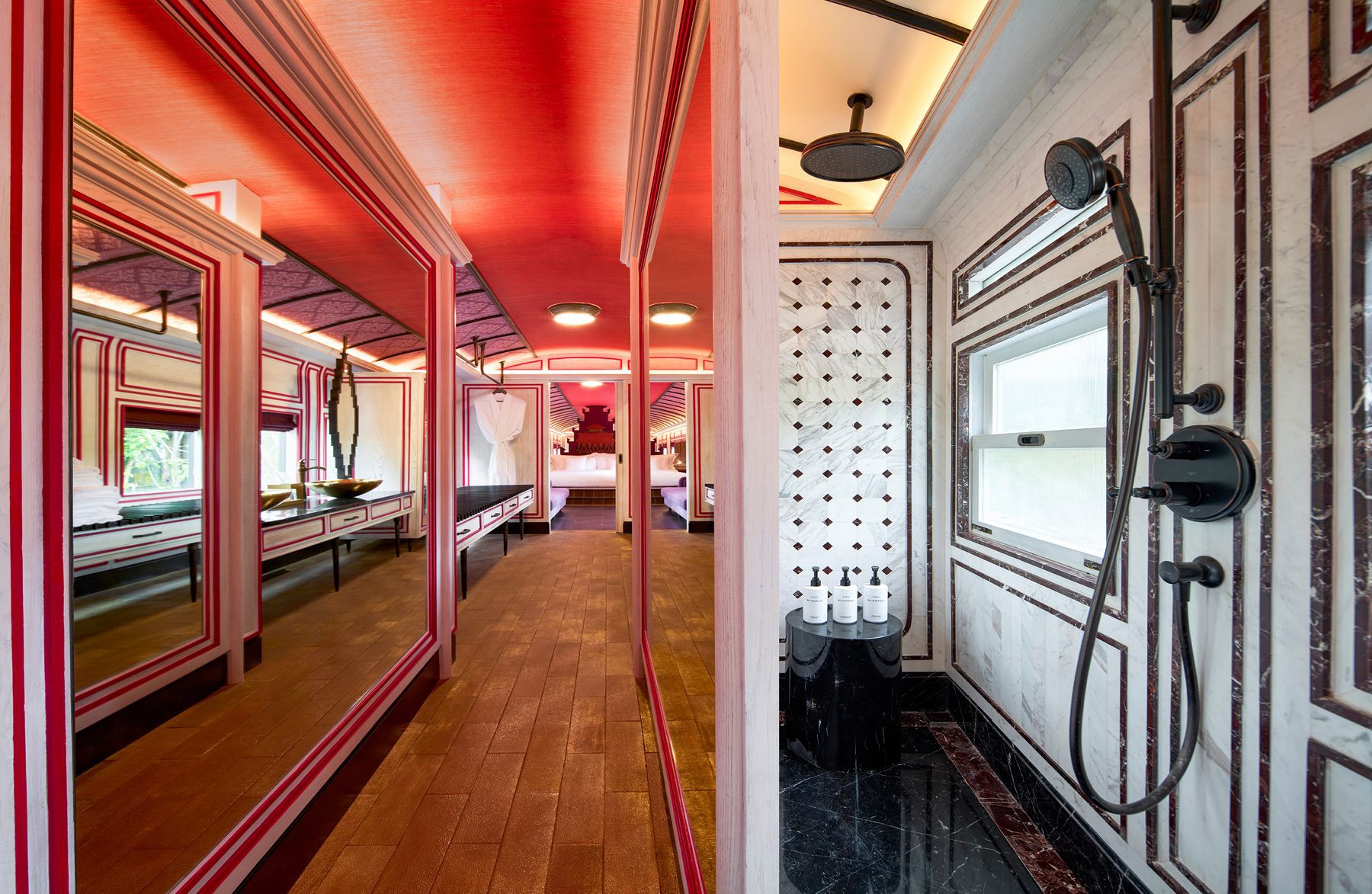 A railcar-style guest room with white and red accents and a bathroom with a KOHLER® Rain Duet Multifunction Handshower.