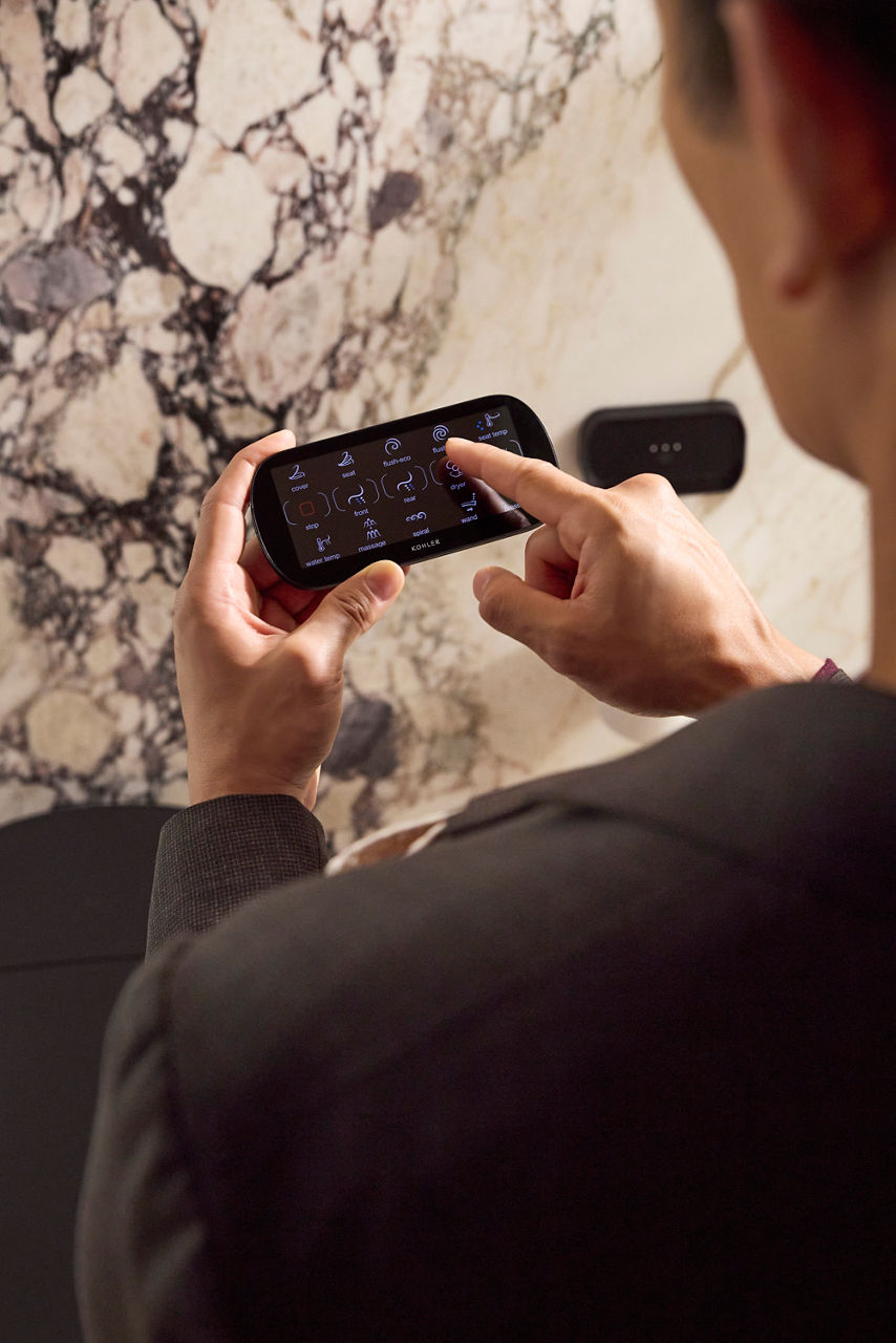 Person operating a handheld touchscreen remote with multiple function icons in a bathroom setting