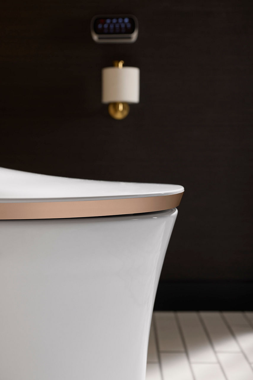Smart toilet with unique color trim on the lid, positioned near a dark wall.