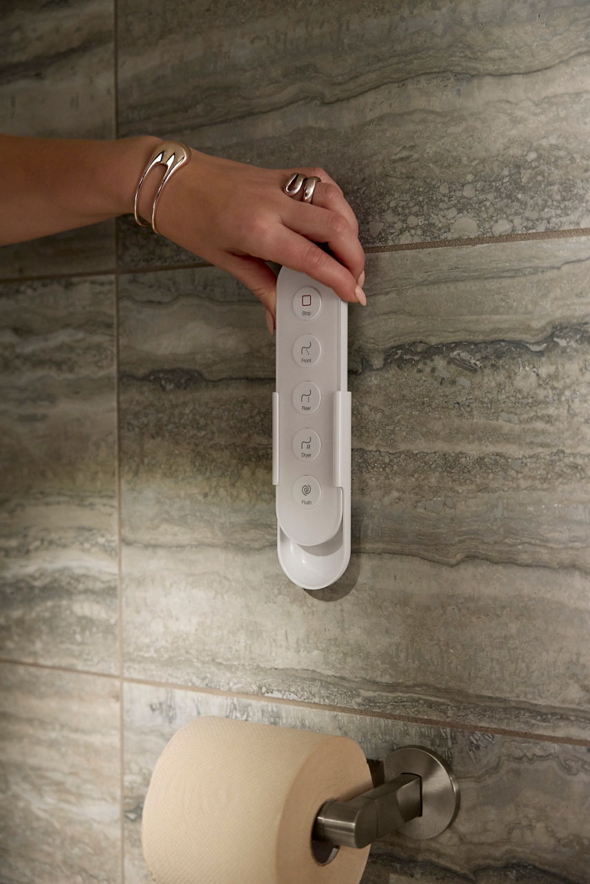 Close-up of a hand using a handheld remote control attached to a tiled bathroom wall