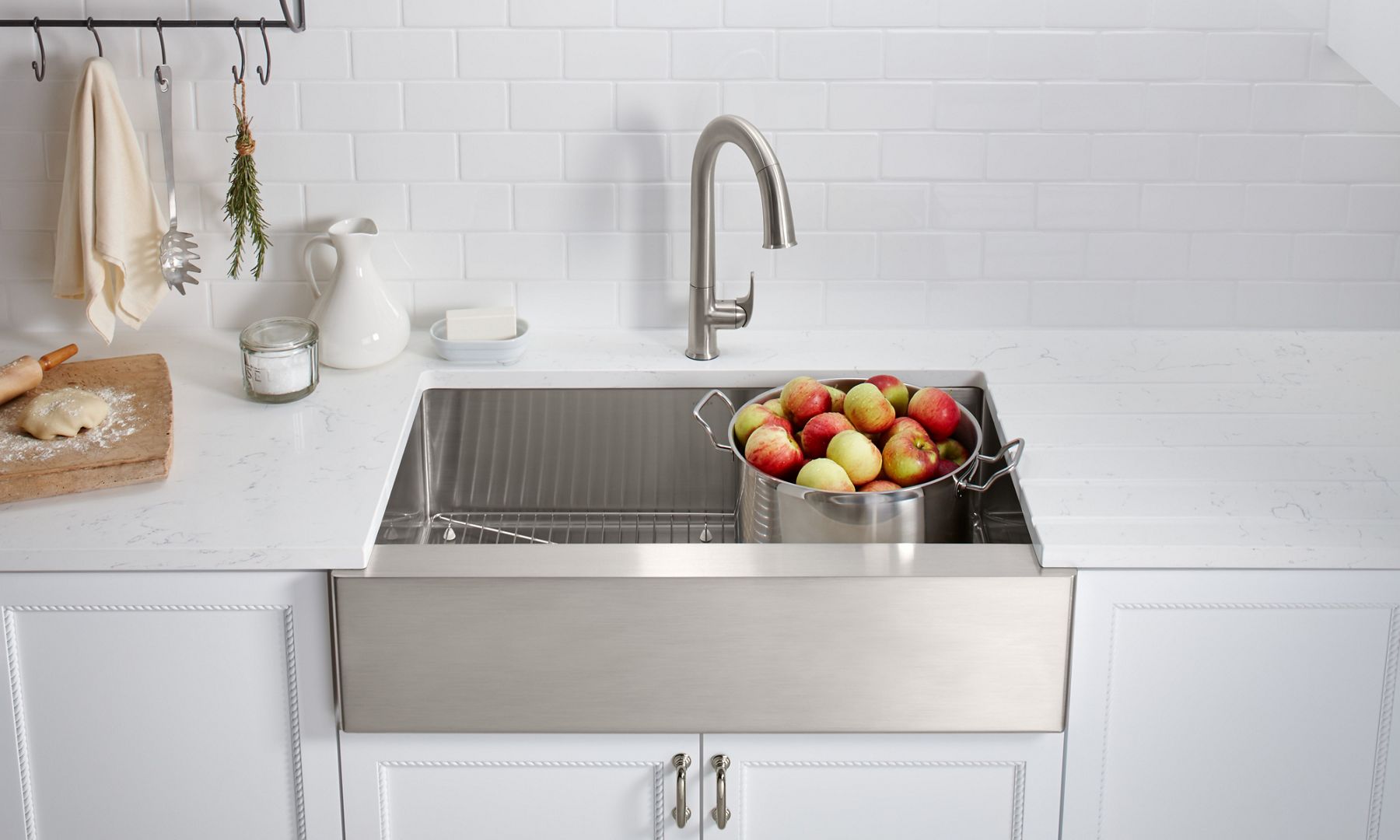 A metal stock pot full of apples sits in a KOHLER Strive stainless steel farmhouse sink.