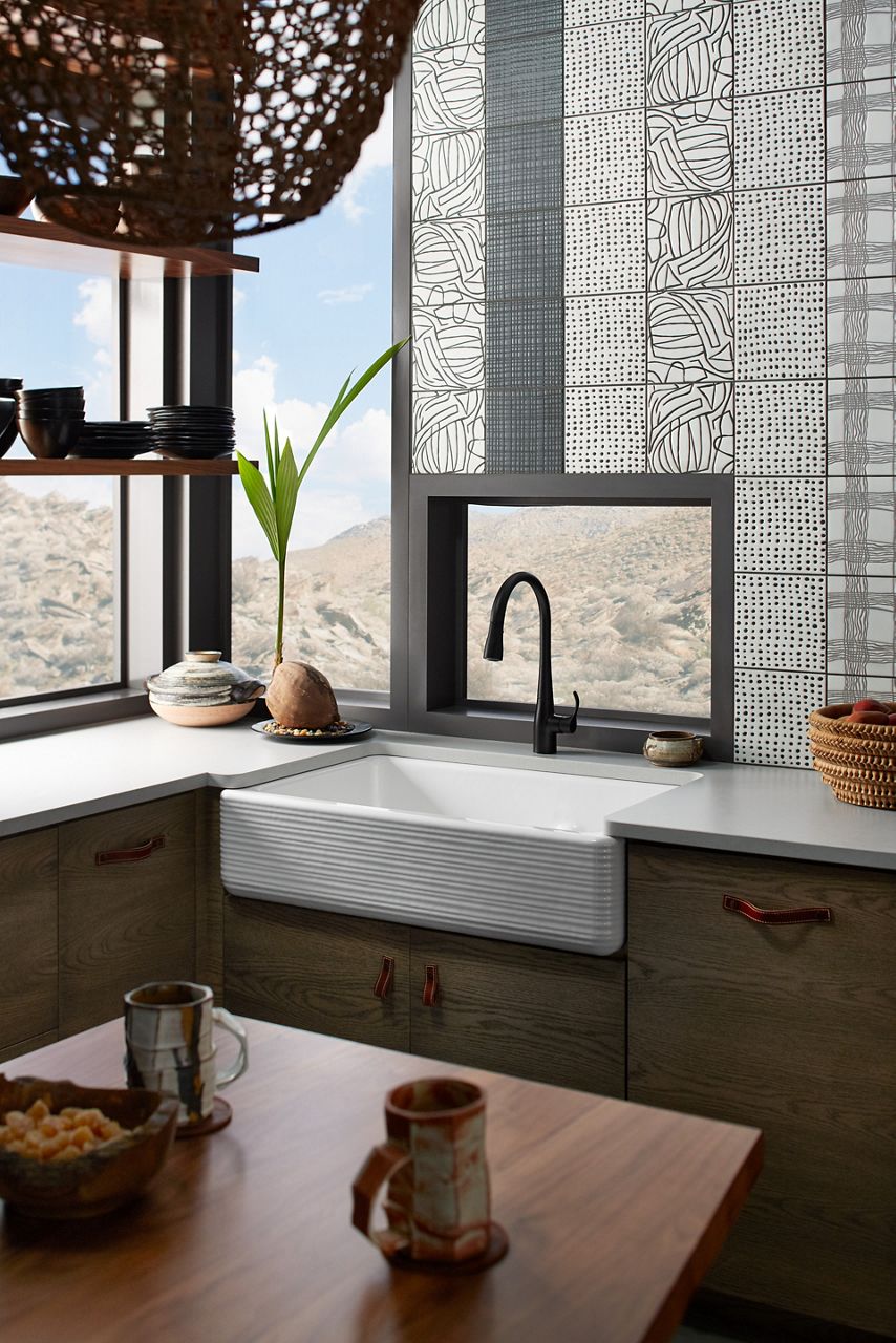 A Whitehaven undermount farmhouse sink in a brown wood-grain cabinet with a light gray counter top and matte black faucet, behind which a window looks out on a desert mountain vista.