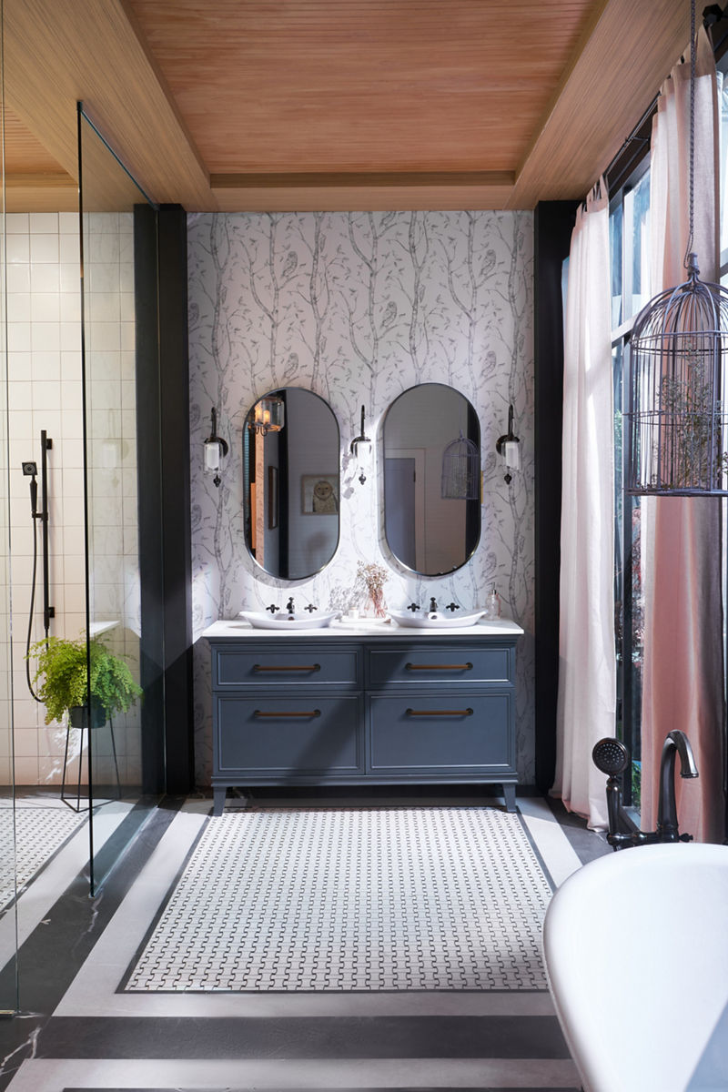 A Harken double vanity in the Slate Grey colorway with wood and matte black handles with double mirrors, sinks and faucets, set against a wallpaper with a tree-like pattern.