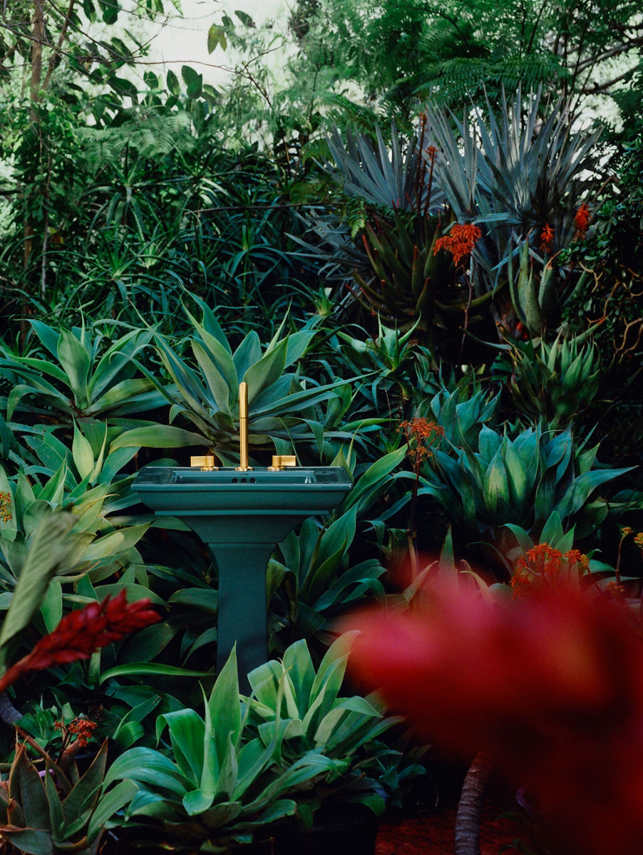 A profile image of a teal bathroom sink with a gold faucet. The sink is positioned in the middle of a garden filled with red flowers.