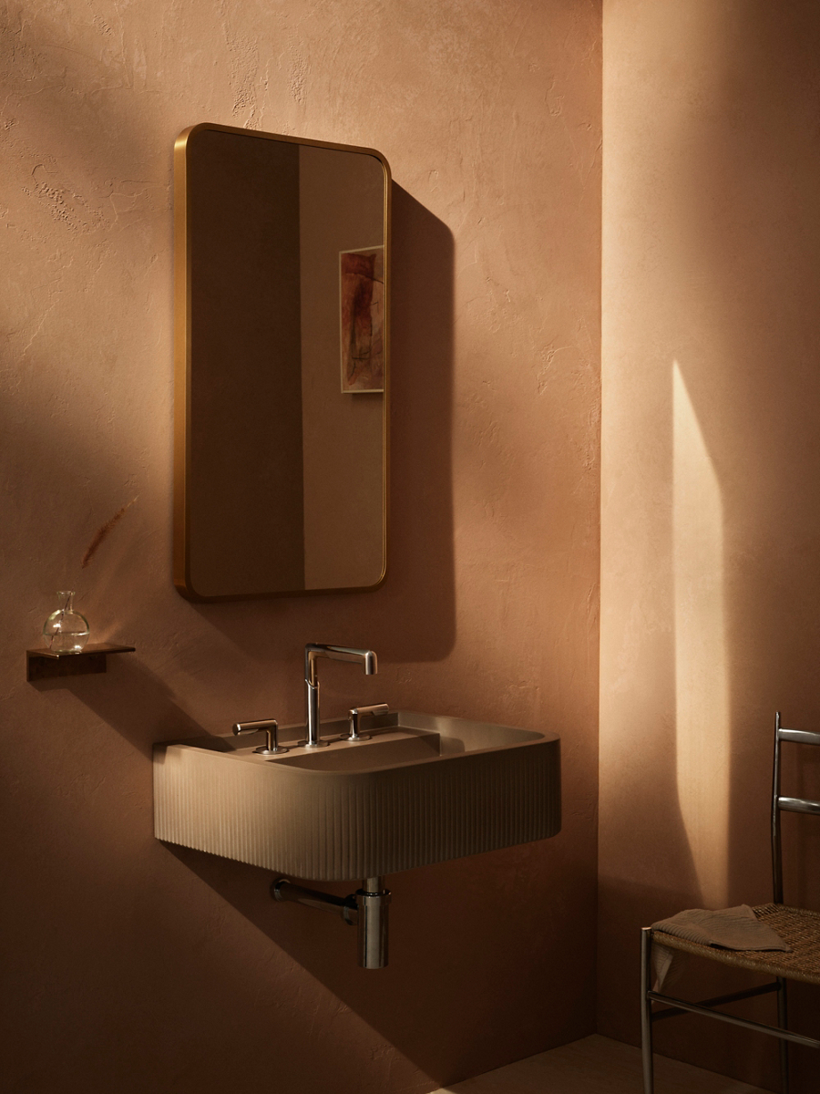 Vice widespread sink faucet with lever handles above a fluted wall-mounted sink and rounded-rectangle mirror.