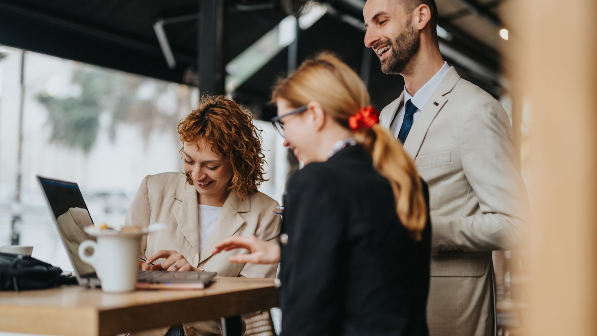 Three professionals engaging in a collaborative discussion while working on a laptop outdoors at a cafe. Represents teamwork, brainstorming, and productivity in a relaxed business environment.