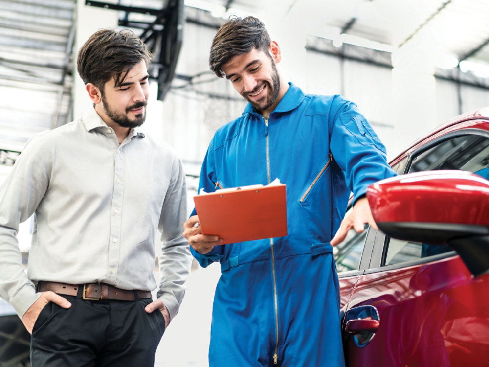 Vehicle maintenance handsome man servicer explain car condition, point at vehicle part to male customer in garage. Automotive mechanic hold automotive checklist document. Car repair service concept.