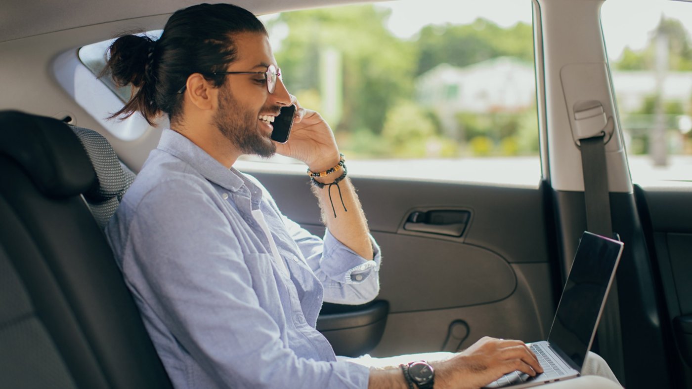 A young man working on the computer on while in the car