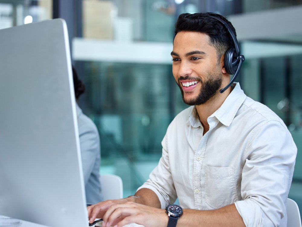 Business man, call center and web support communication at a computer in a office. Phone conversation, smile and male worker with contact us, crm and customer service job in a consulting agency.