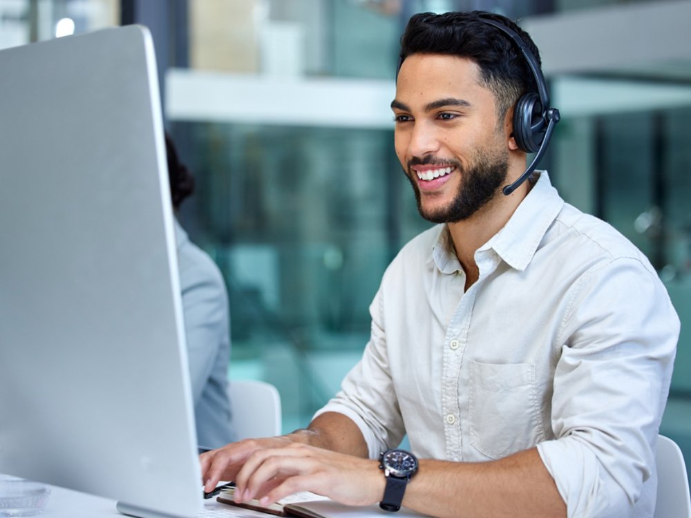 Business man, call center and web support communication at a computer in a office. Phone conversation, smile and male worker with contact us, crm and customer service job in a consulting agency.