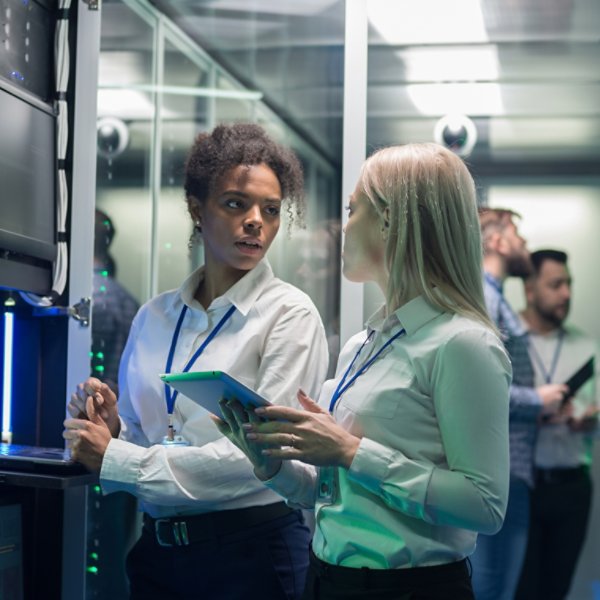 Medium shot of two women working in a data center with rows of server racks and checking the equipment and discussing their work