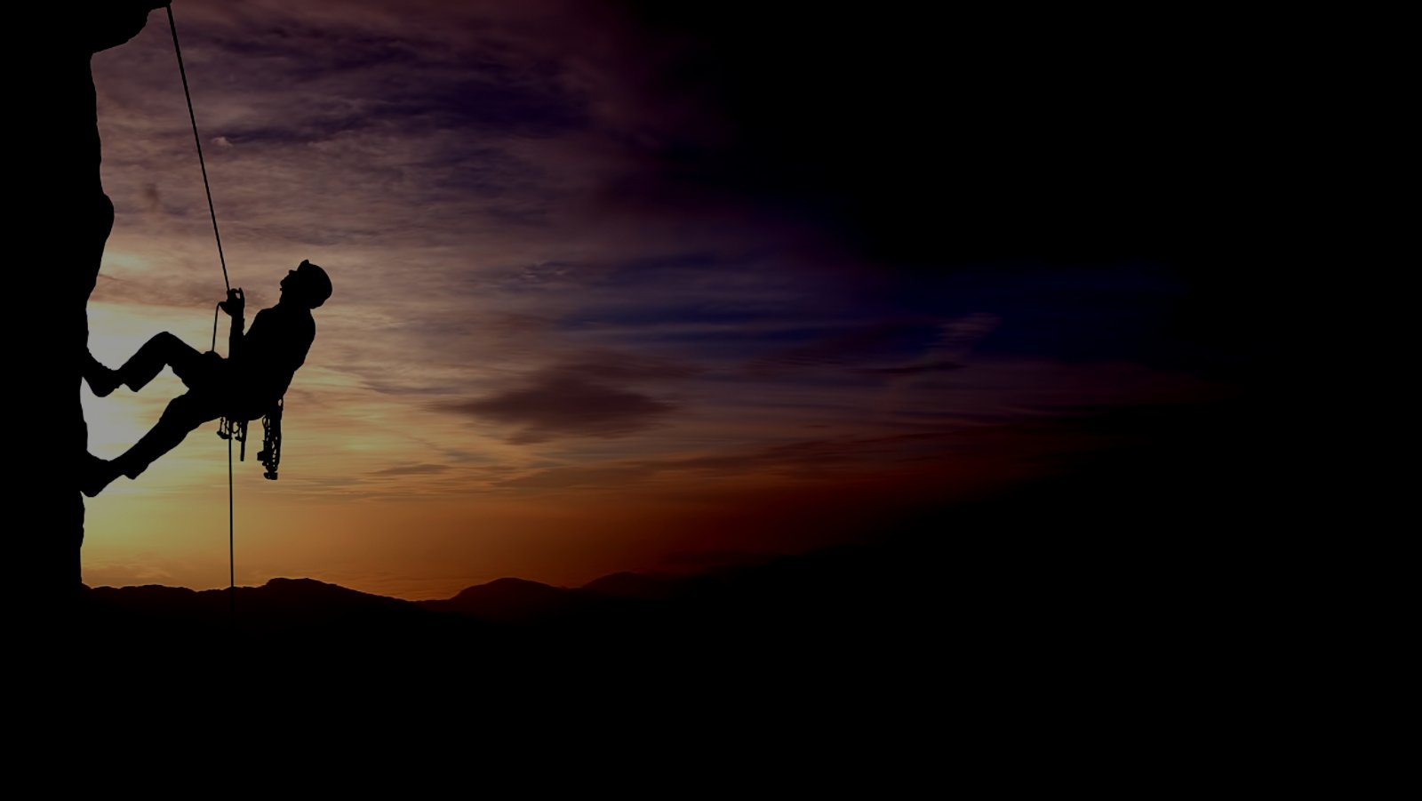 Silhouette of a climber on a vertical wall over beautiful sunset