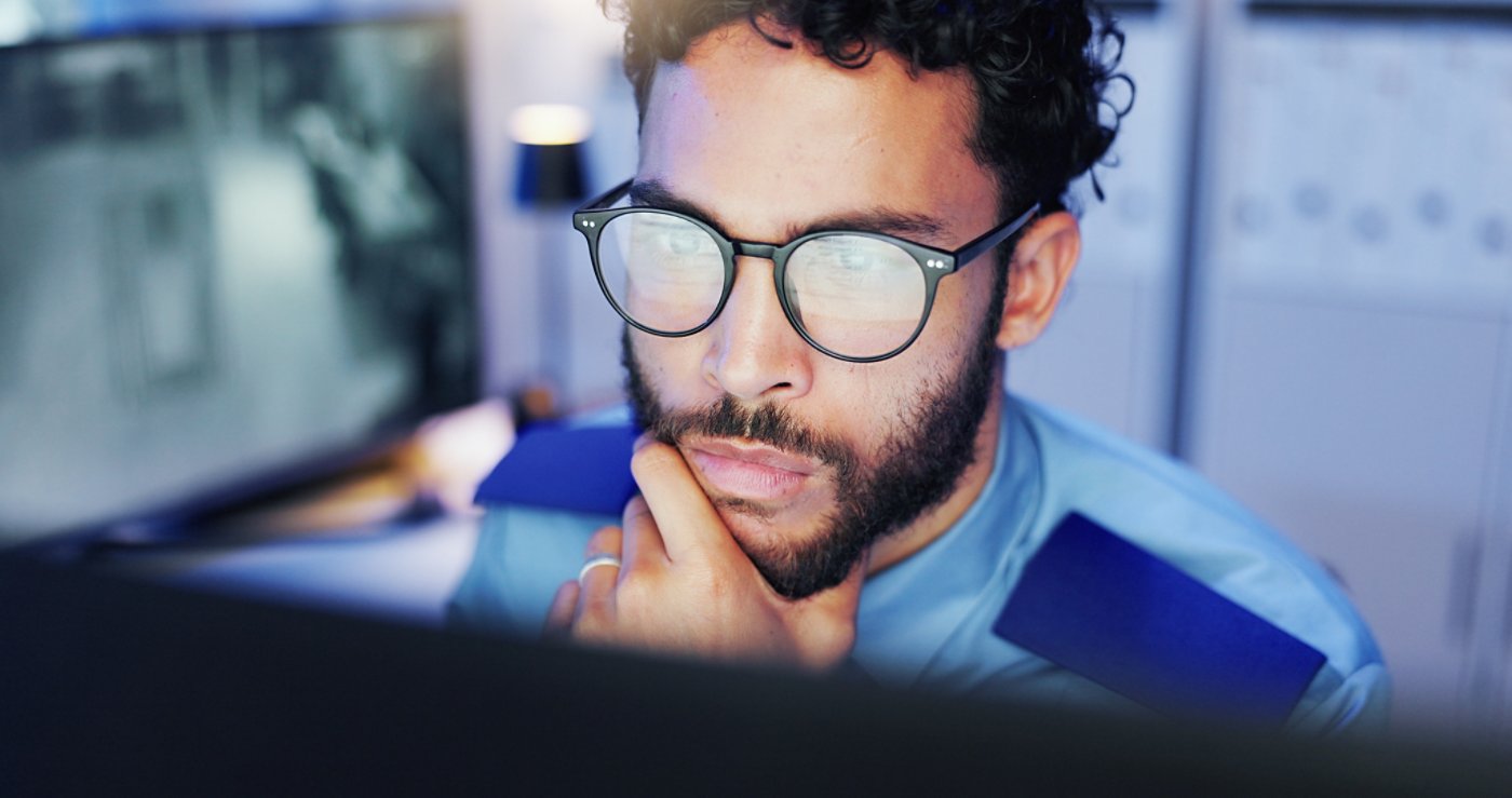 Night, footage and security guard with computer, man and monitoring of danger with tech and safety. Watching, video and person with glasses in control room, protection and serious for observation.