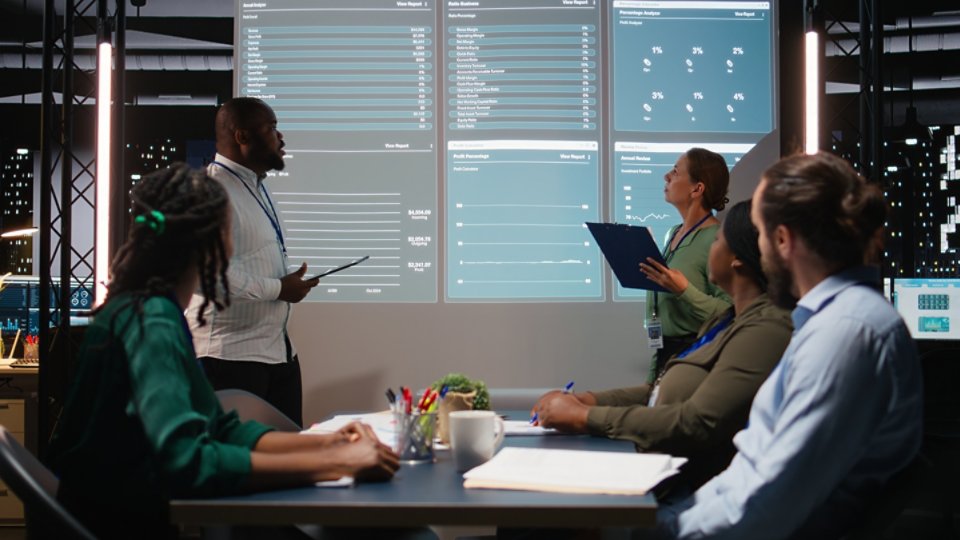 Diverse business associates reviewing performance metrics data within the multinational company. Conducting analytics for general overview, professional development after hours. Camera A.