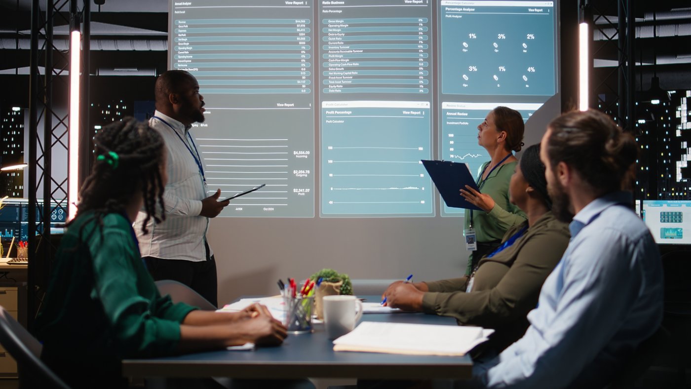 Diverse business associates reviewing performance metrics data within the multinational company. Conducting analytics for general overview, professional development after hours. Camera A.