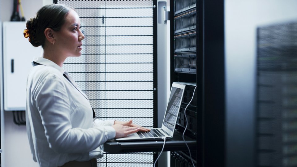 Laptop, typing and woman in server room for engineering, network maintenance or programming. Administration, computer and cybersecurity with IT professional in data center for firewall installation.
