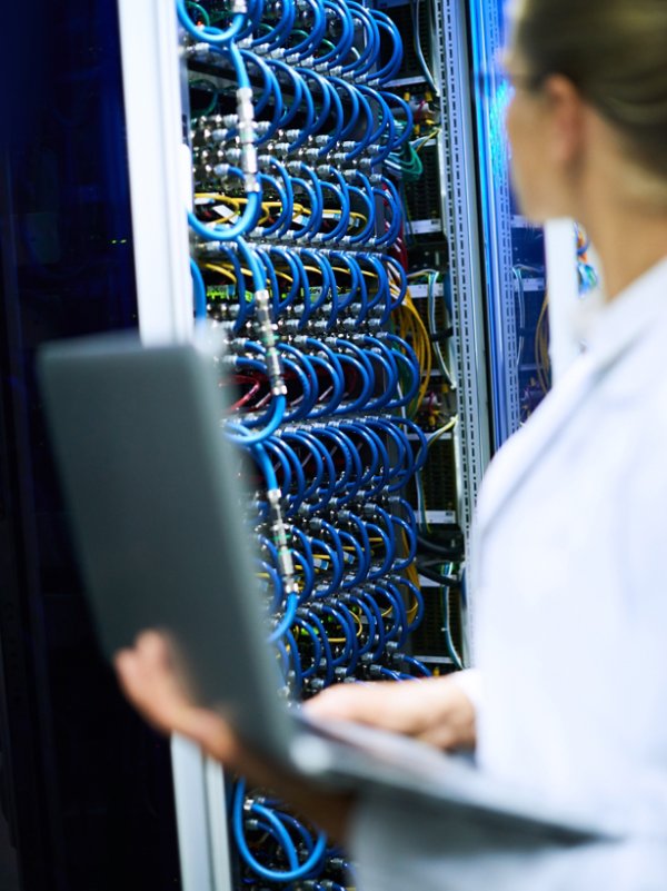 Unrecognizable female scientist working with supercomputer, focus on server cabinet with wires in background