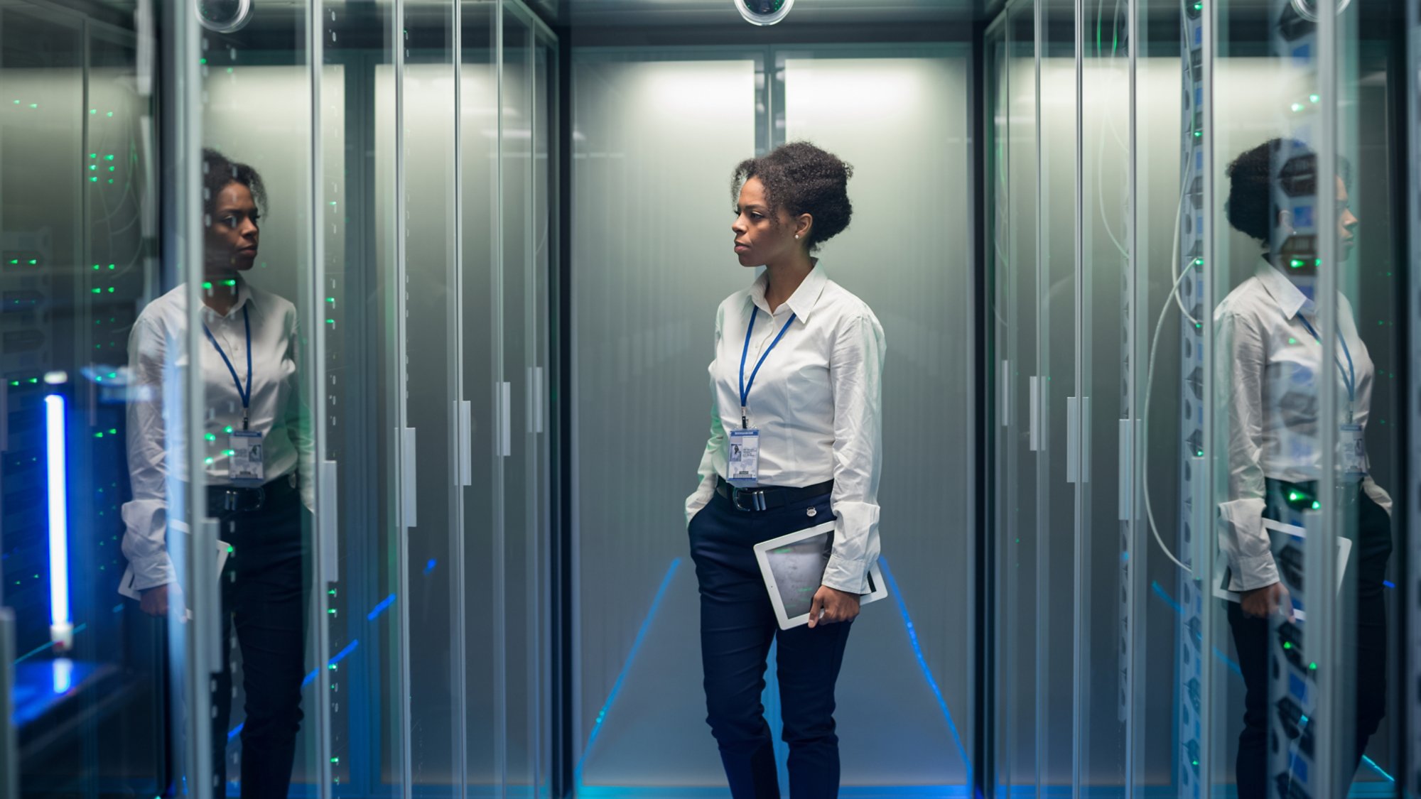 African American woman with tablet while walking in corridor of data center and checking hardware on server racks