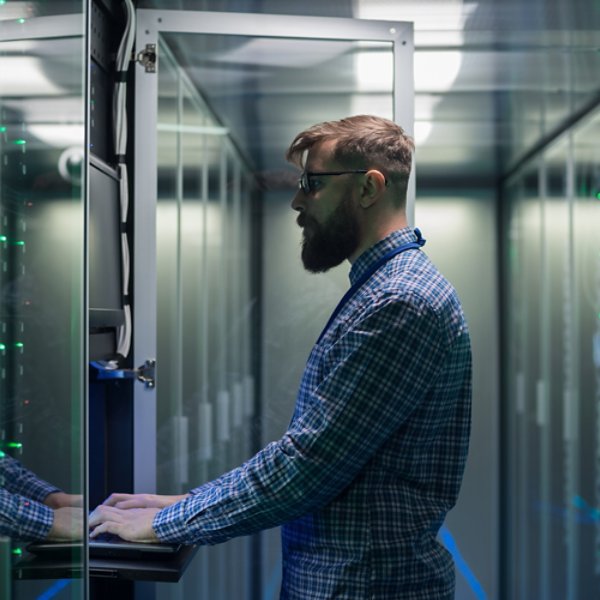 Adult bearded system administrator in glasses working on laptop and correcting errors in server hardware