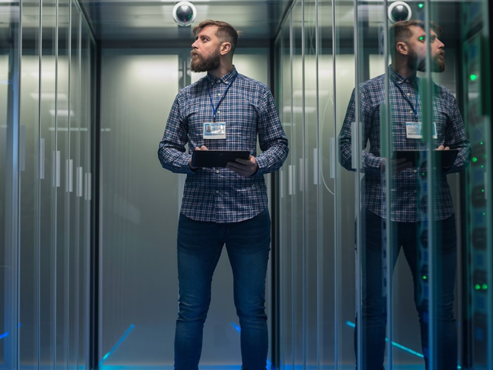 Portrait of adult bearded man and woman standing in corridor of server room in data center smiling at camera