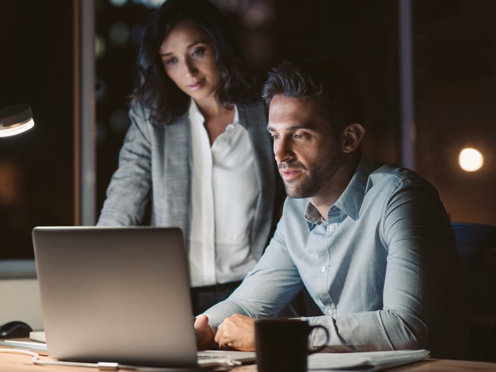 Businesspeople working together on a laptop late in the evening