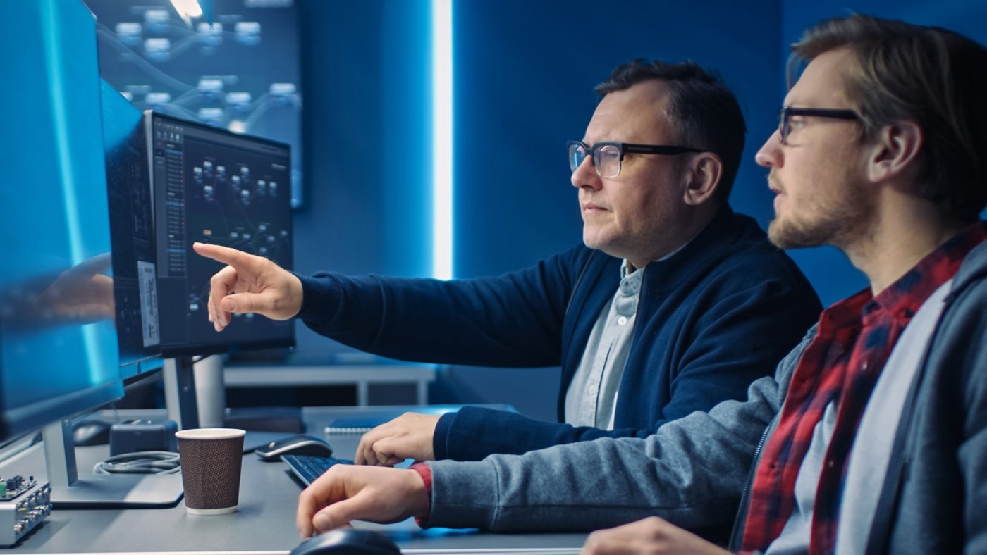 Two Professional IT Programers Discussing Blockchain Data Network Architecture Design and Development Shown on Desktop Computer Display. Working Data Center Technical Department with Server Racks 