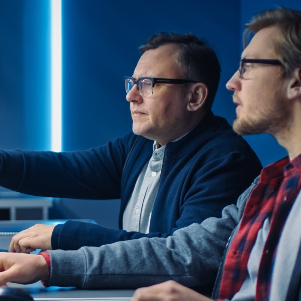 Two Professional IT Programers Discussing Blockchain Data Network Architecture Design and Development Shown on Desktop Computer Display. Working Data Center Technical Department with Server Racks 