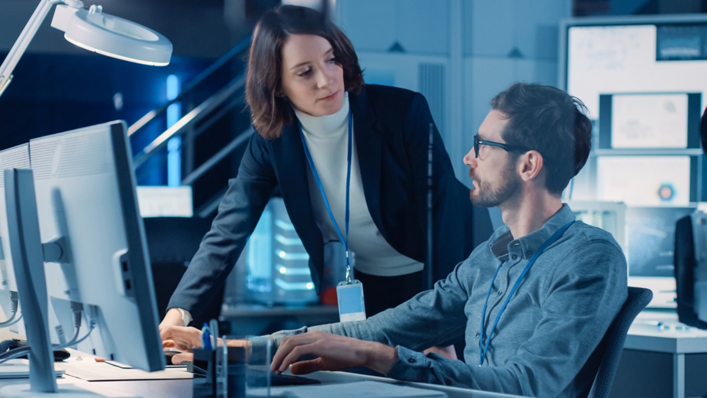 Futuristic Machine Engine Development Engineer Working on Computer at His Desk, Talks with Female Project Manager. Team of Professionals Working in the Modern Industrial Design Institution