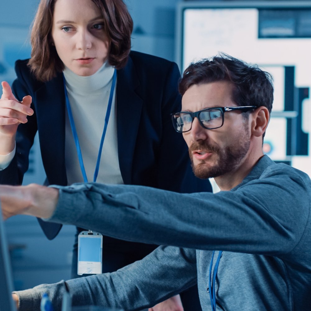 Futuristic Machine Engine Development Engineer Working on Computer at His Desk, Talks with Female Project Manager. Team of Professionals Working in the Modern Industrial Design Institution