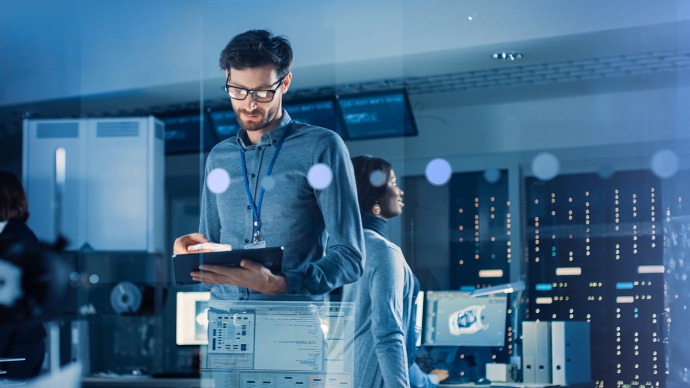 In Technology Research Facility: Chief Engineer Stands in the Middle of the Lab and Uses Tablet Computer. Team of Industrial Engineers, Developers Work on Engine Design Use Digital Whiteboard and Computers