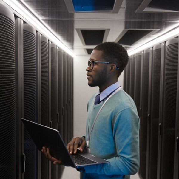 Side view portrait of young African American data engineer working with supercomputer in server room and holding laptop, copy space