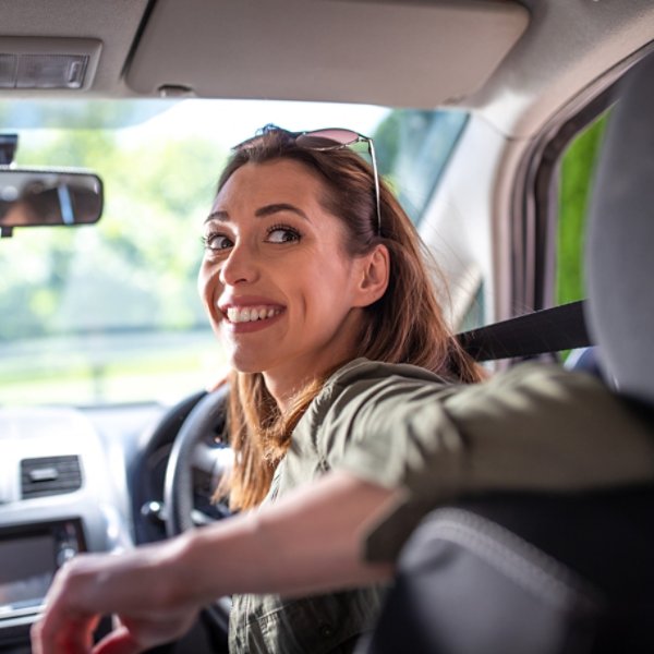 Pretty young woman driving car smiling. Attractive woman going in reverse looking back over shoulder. 