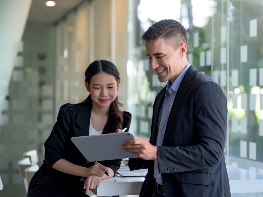 Two business people discuss investment project working and planning strategy. Businessman and businesswoman talking together with tablet at office.