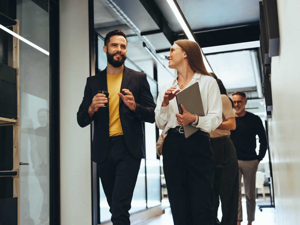 Young professionals having a discussion in a modern office. Two happy young businesspeople smiling while walking together in a hallway. Cheerful colleagues collaborating on a new project.