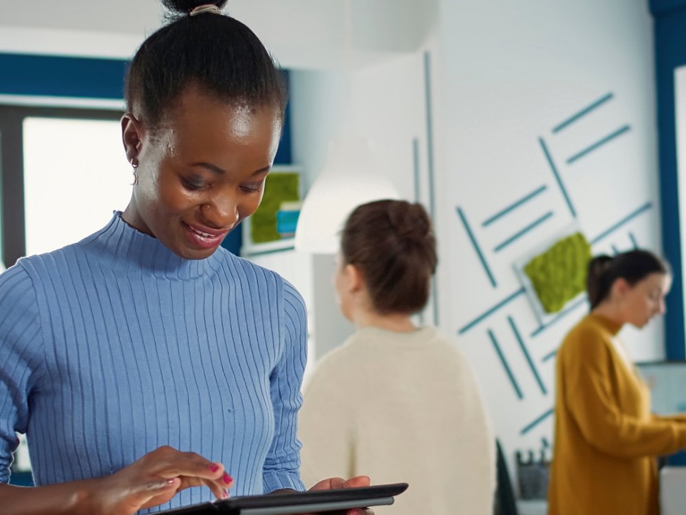 Portrait of african american woman standing in busy office picking up tablet with business erp software and smiling