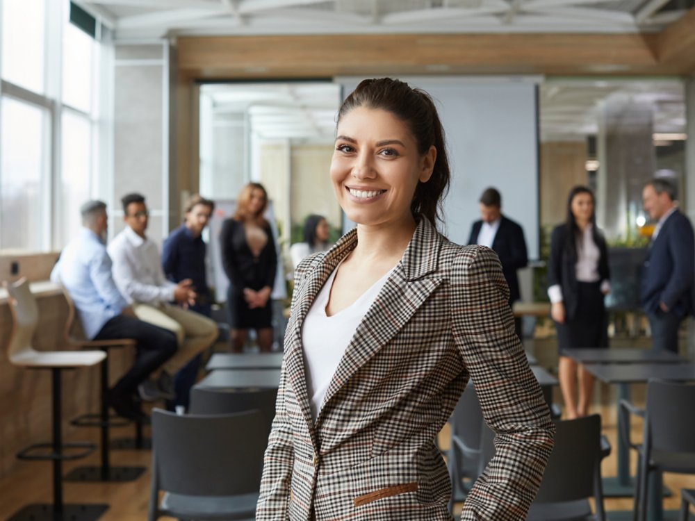 Portrait of happy female business teacher and professional coach. Beautiful young woman in jacket standing in office after corporate training class for team of employees, looking at camera and smiling