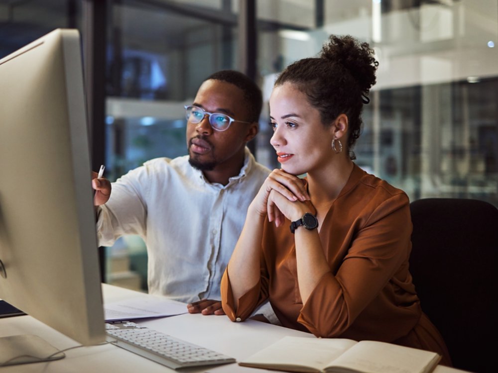 Business training, night planning and employees talking about corporate proposal on internet in dark office at night. African workers working on partnership on the web with computer during overtime.