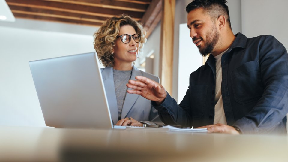 Business man having a discussion with his colleague in an office. Two business people using a laptop in a meeting. Teamwork and collaboration between business professionals.