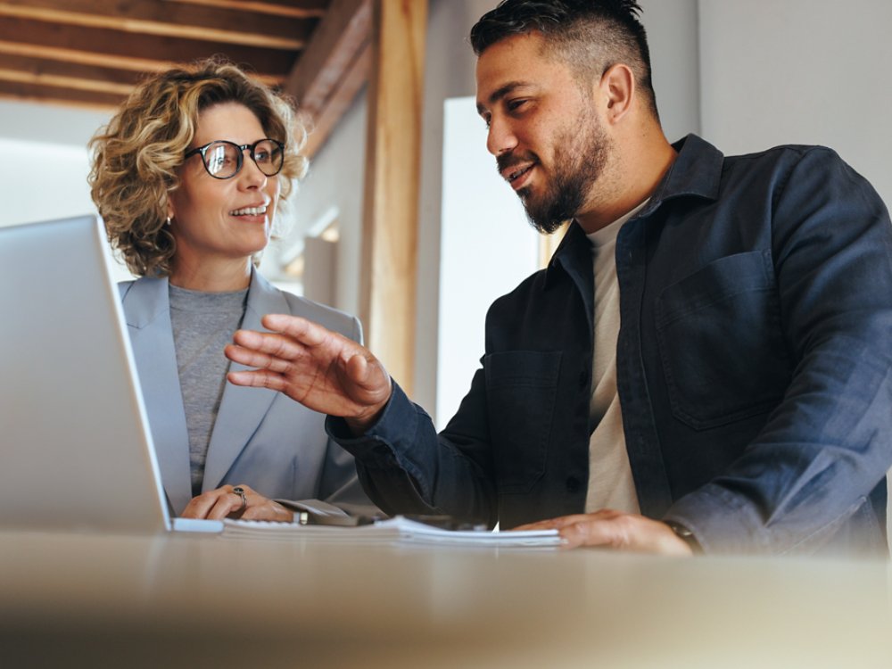 Business man having a discussion with his colleague in an office. Two business people using a laptop in a meeting. Teamwork and collaboration between business professionals.