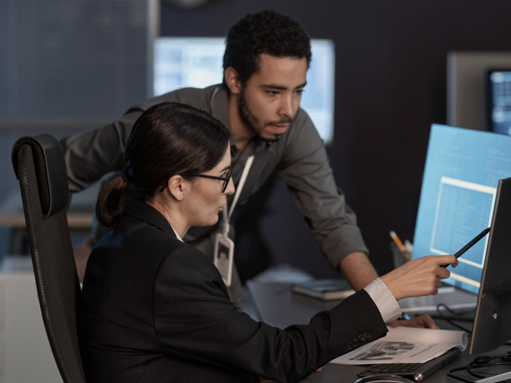 Two people pointing at computer screen while working in IT company