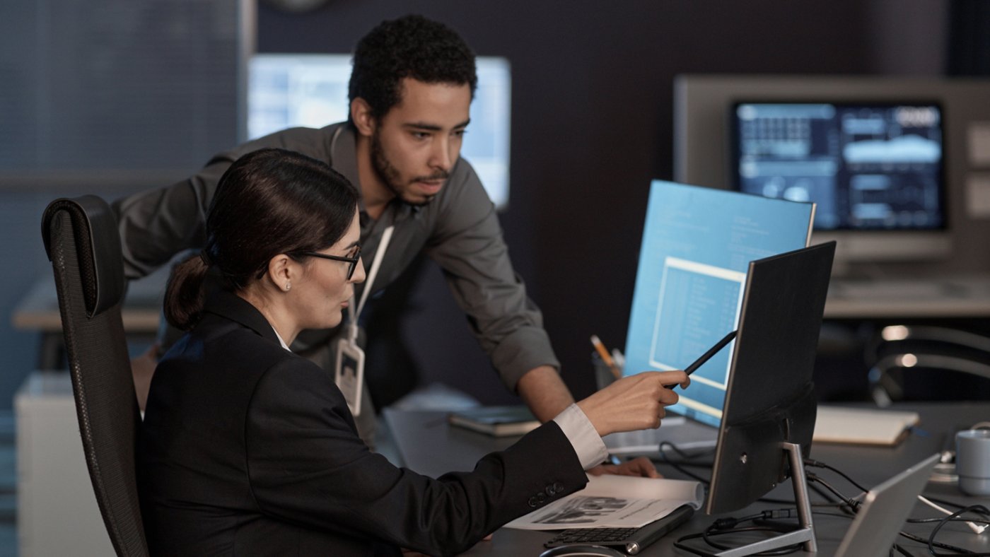 Two people pointing at computer screen while working in IT company