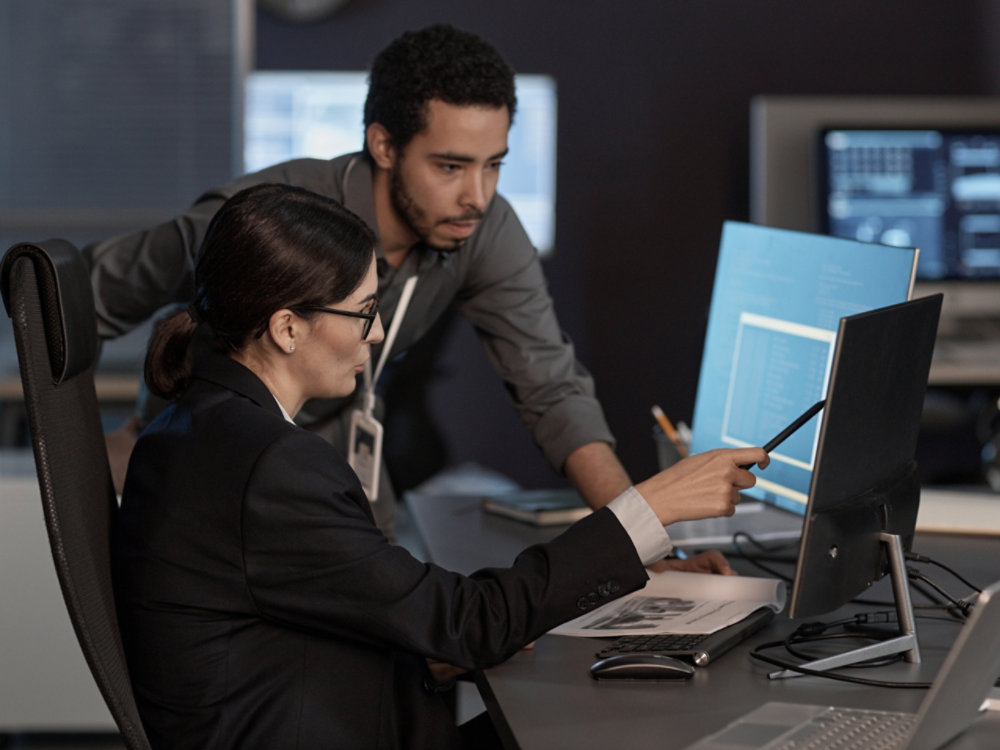 Two people pointing at computer screen while working in IT company