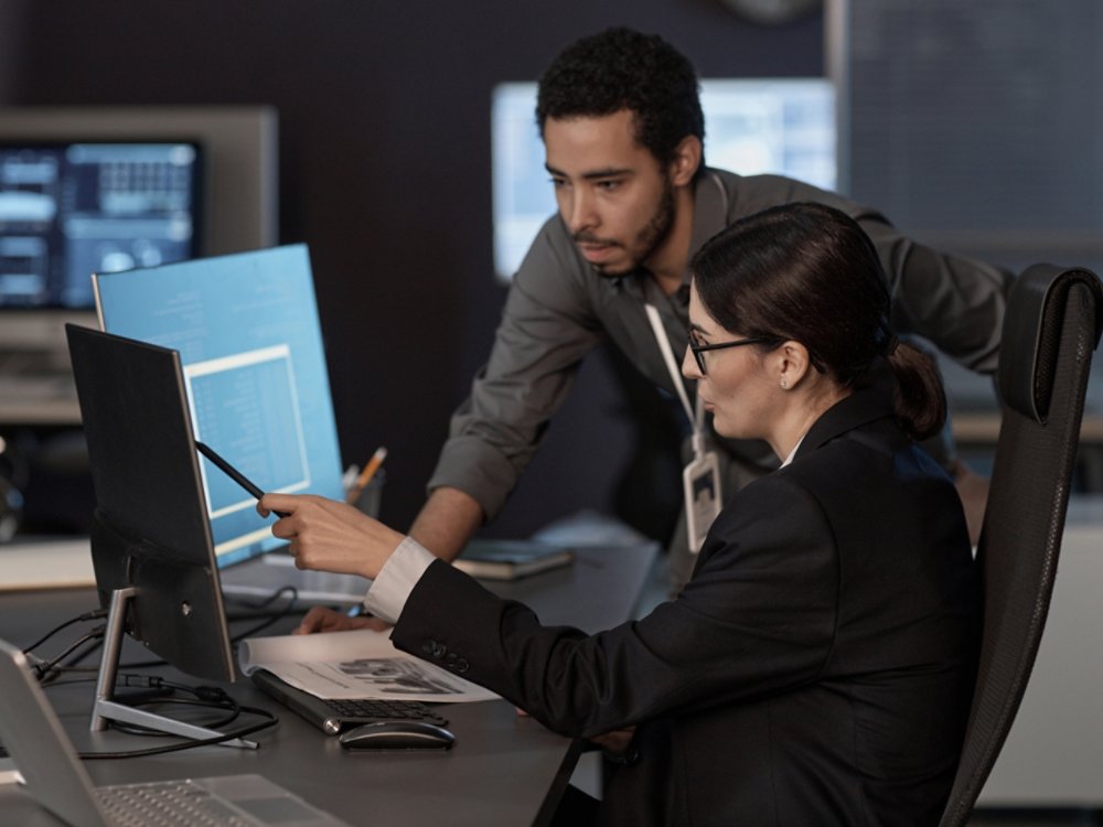 Two people pointing at computer screen while working in IT company