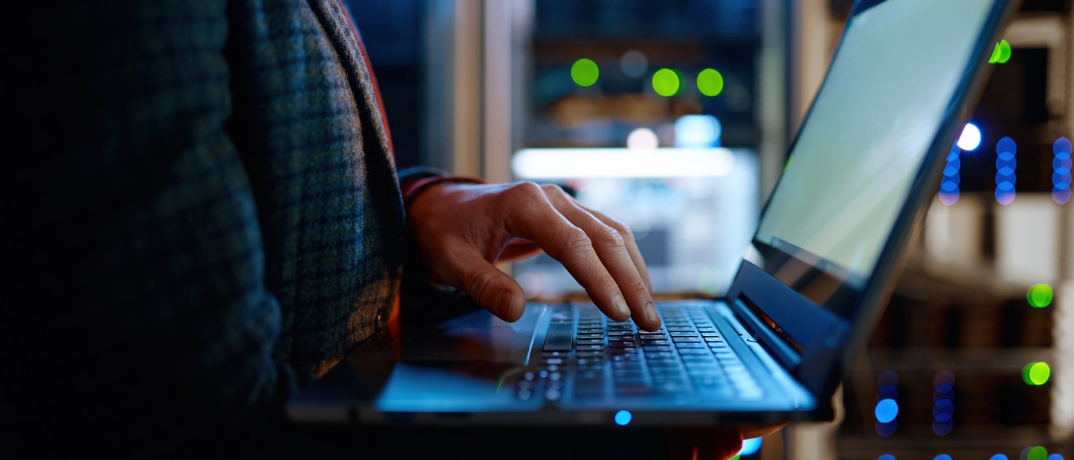 IT technician checking the servers vitals using laptop computer. Male support agent working in a dark network server room