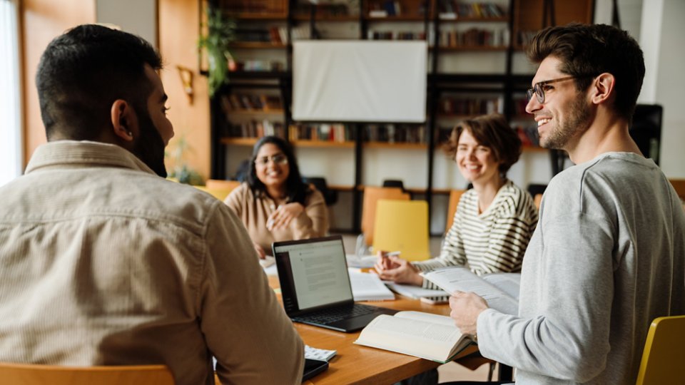 Group of cheerful young multiethnic students in casual wear working on university project in college library