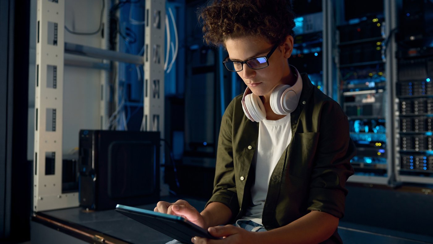 Teenager guy IT technician working on tablet inside server room