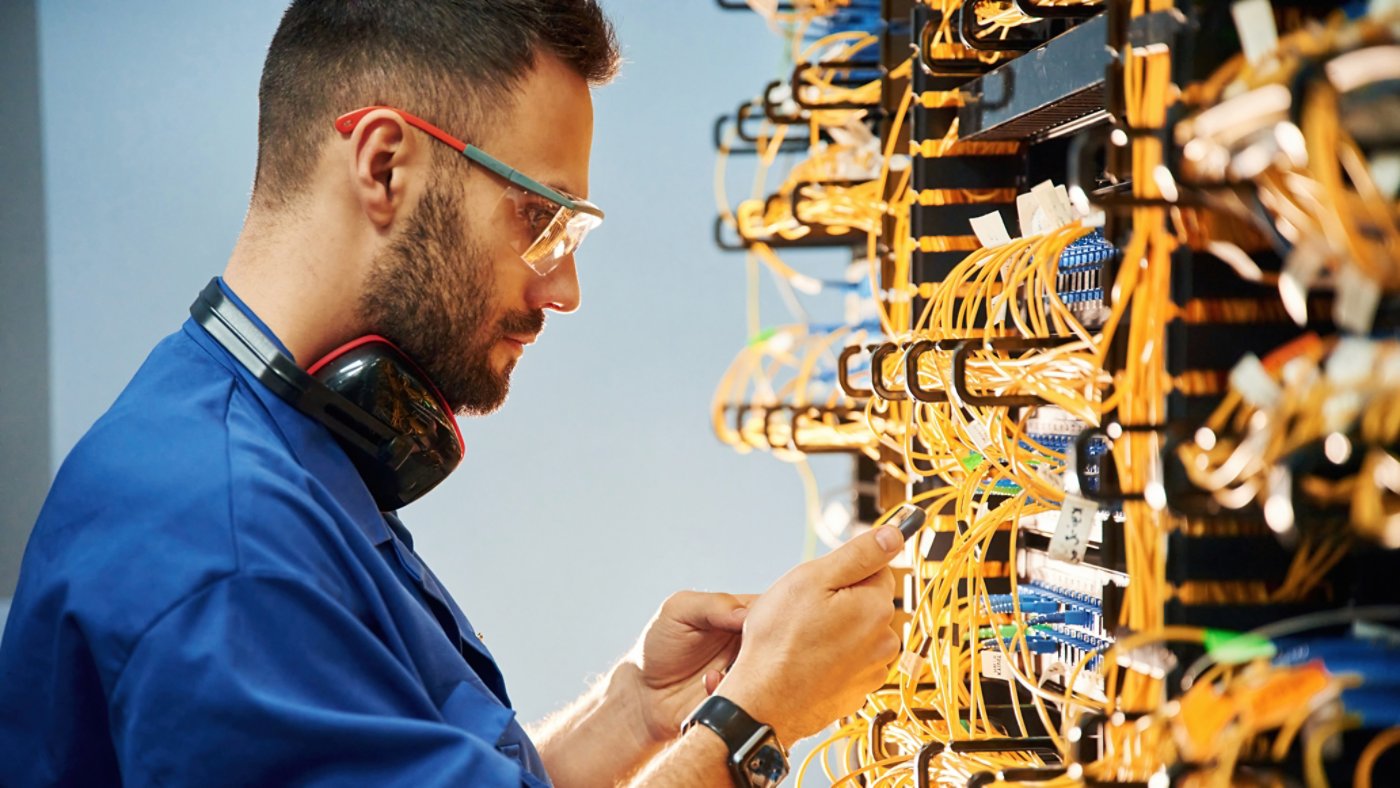 Side view. Young man is working with internet equipment and wires in server room